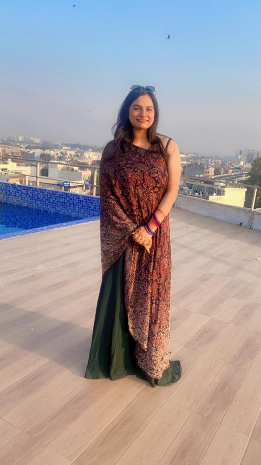 Woman standing on a rooftop with a cityscape view, wearing a patterned dress.